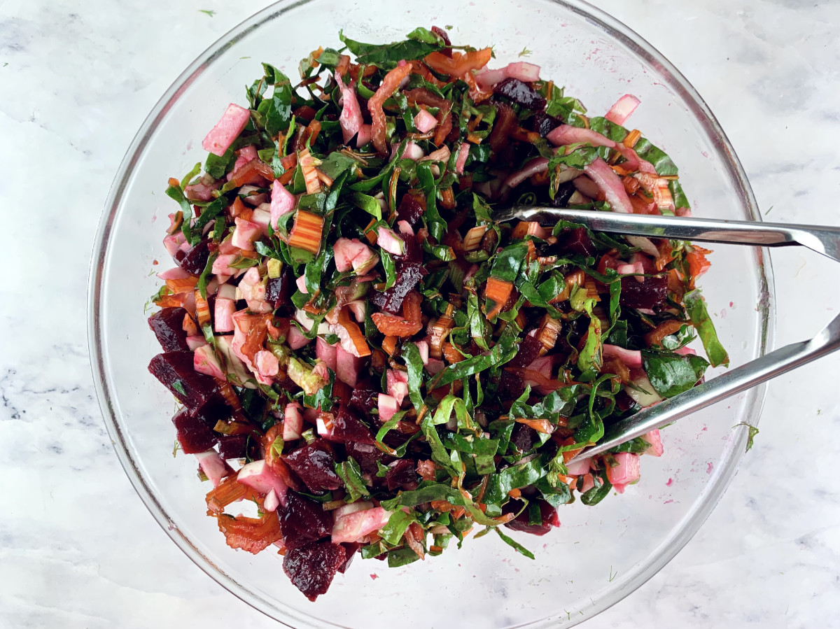 Mixing vegan beet salad in a glass bowl with tongs.