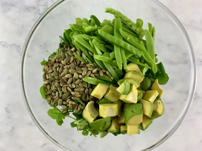 Prepared snow pea salad ingredients in a glass bowl.