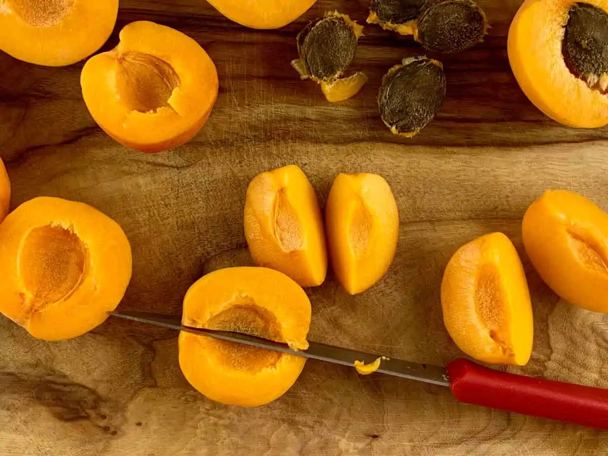 A knife quartering apricots on a wooden board.