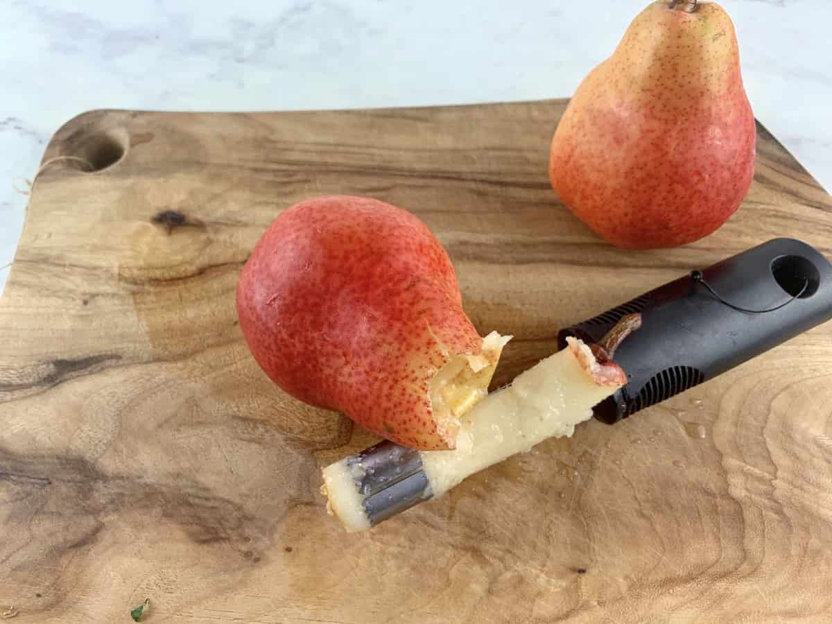 Removing pear cores with a corer on a wooden board.