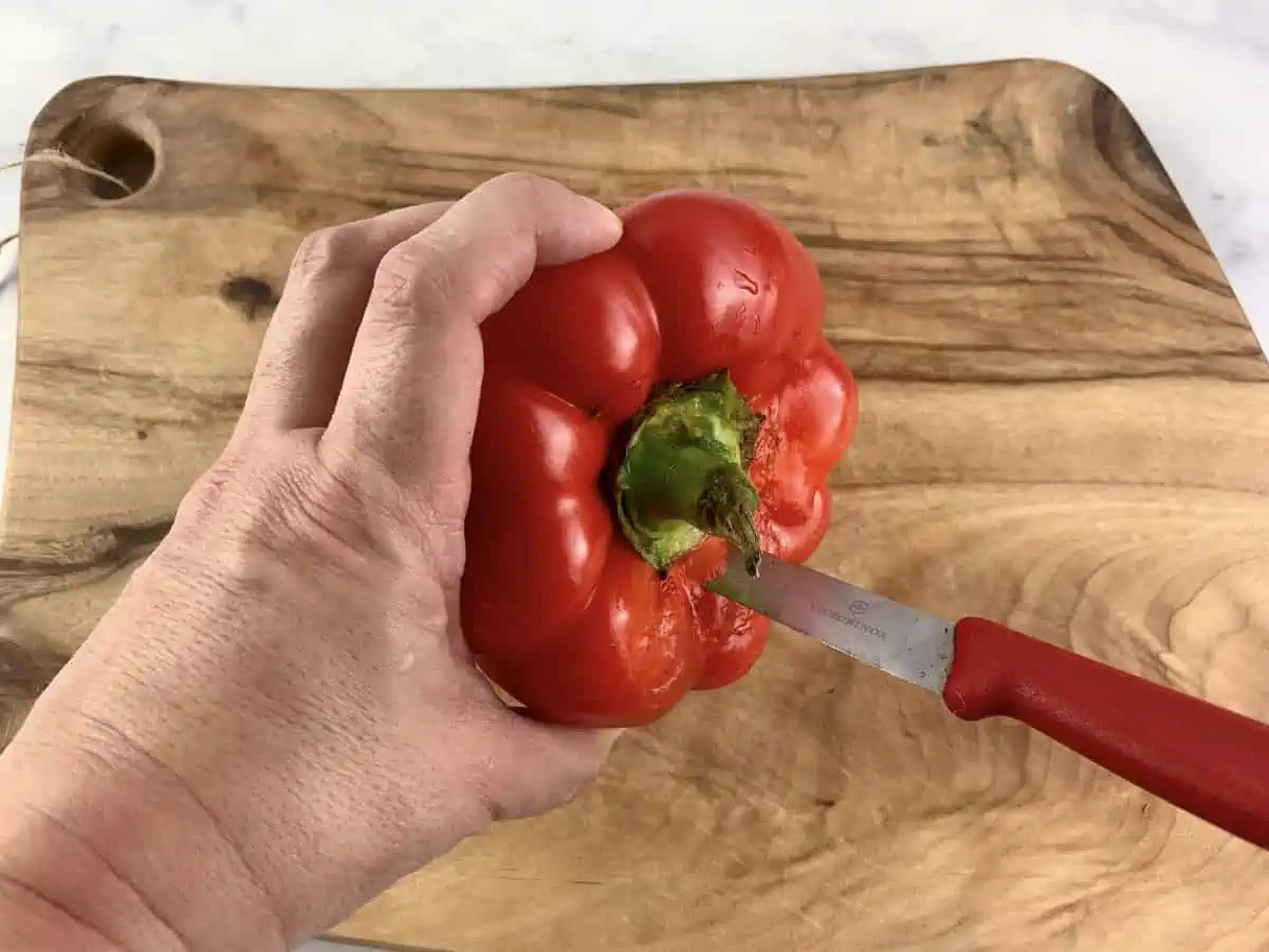 Hands removing core from a red pepper on a wooden board.