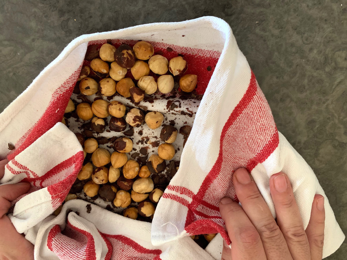 Hands rubbing hazelnuts in a towel to remove their skins.