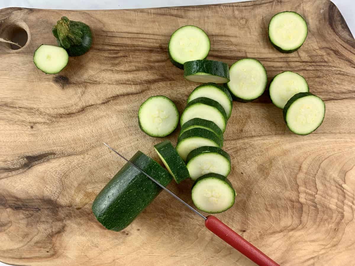 A knife slicing zucchini into rounds on a wooden board.