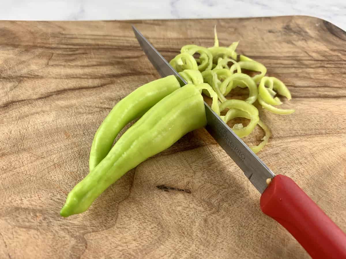 Slicing banana peppers on a wooden board with a knife.