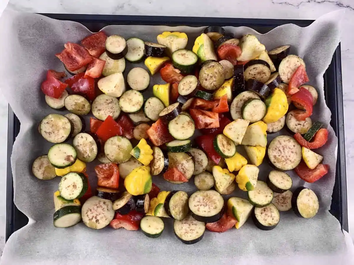 Cut and seasoned vegetables on a lined baking tray.