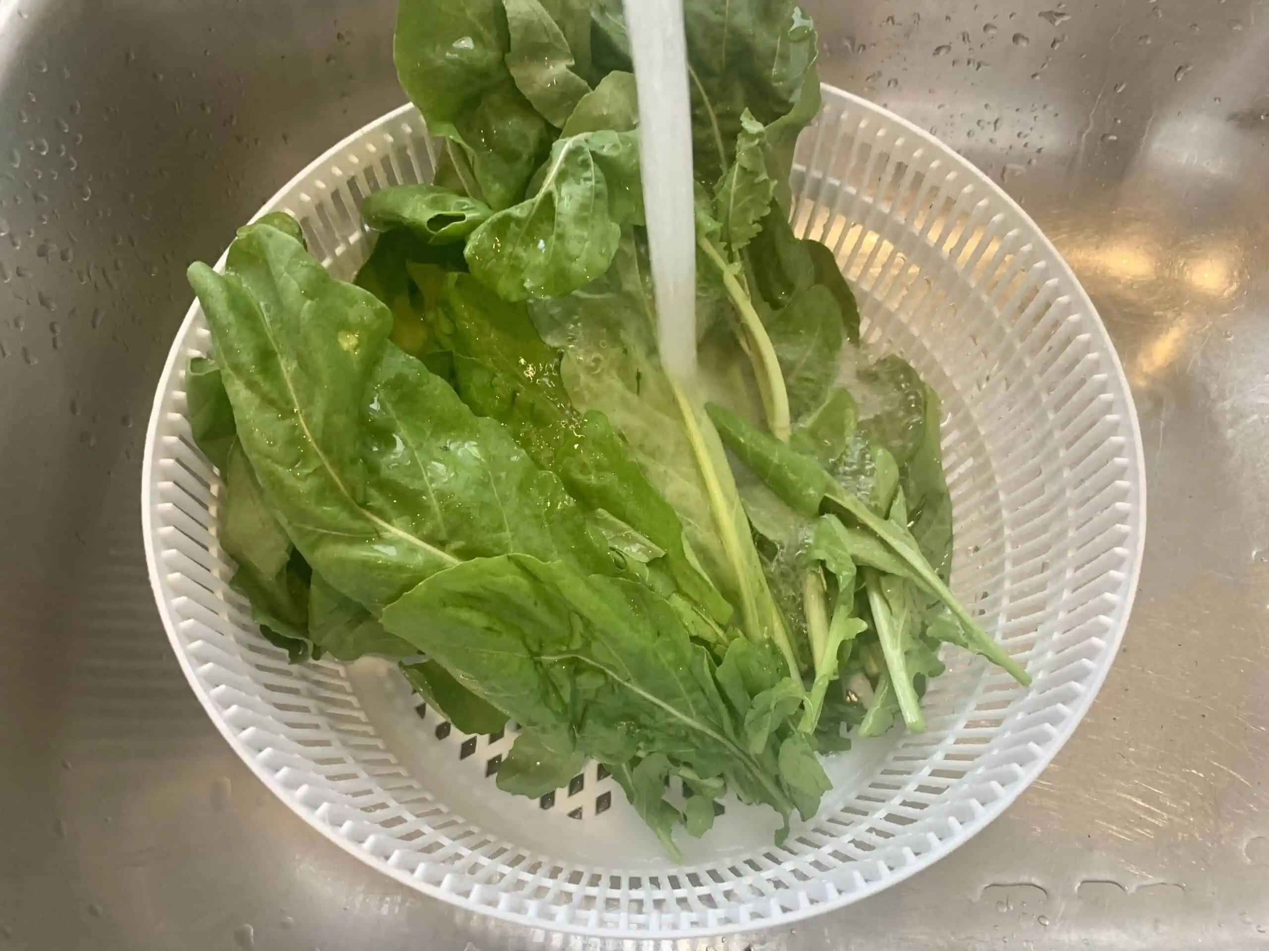 Washing a bunch of rocket in a colander in the sink under cold running water.