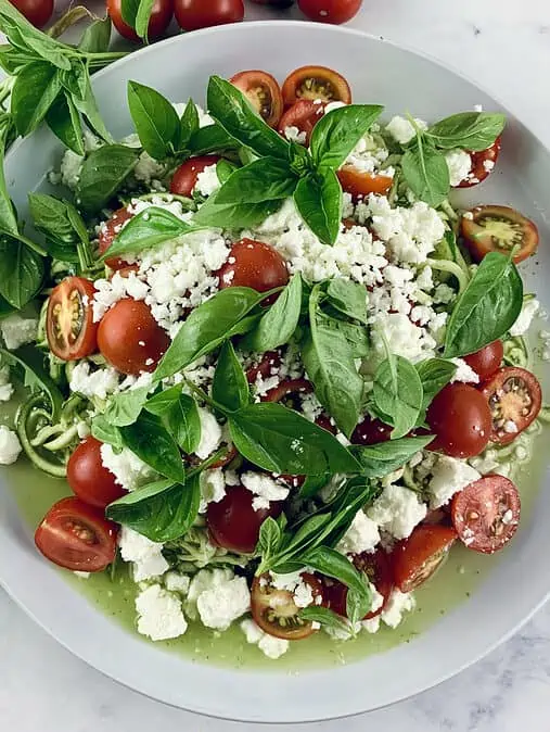 A close-up of zucchini tomato salad with feta on a white plate.
