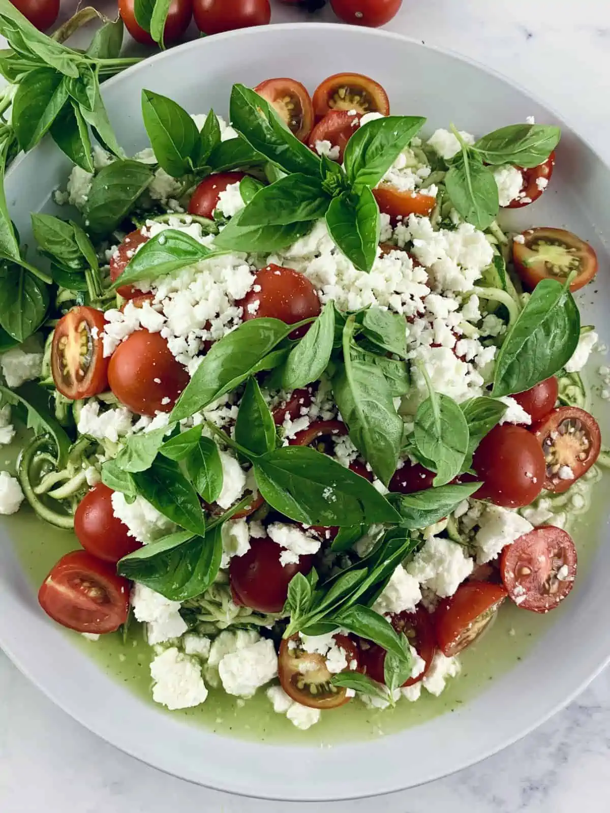 A close-up of zucchini tomato salad with feta on a white plate.