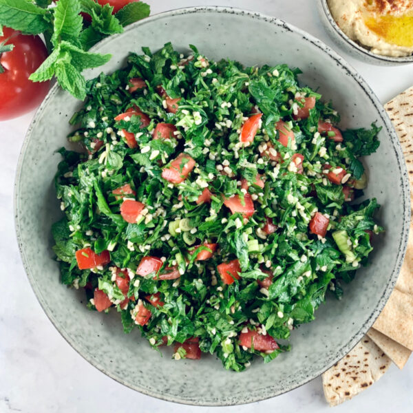 Lebanese tabbouleh in a ceramic bowl with tomatoes, hummus and pita bread on the side.