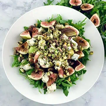 Arugula Fig Salad in a white bowl with arugula, and halved figs on the side.