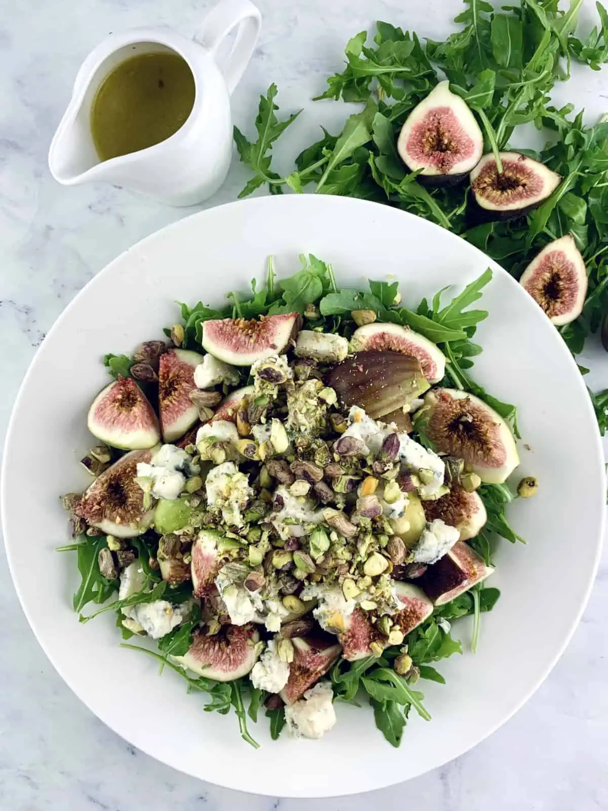 Arugula Fig Salad in a white bowl with arugula, halved figs and dressing on the side.