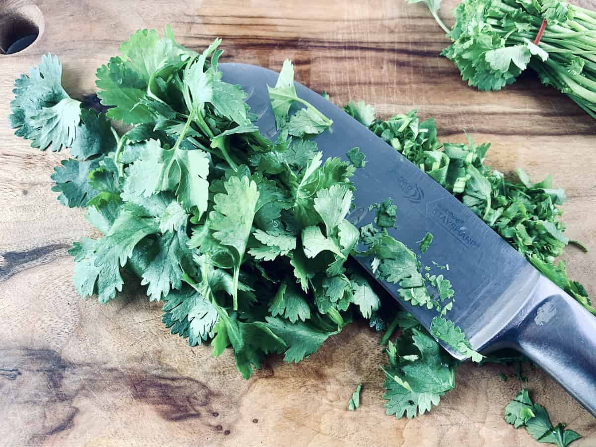 Chopping coriander, cilantro on a wooden board with a knife.