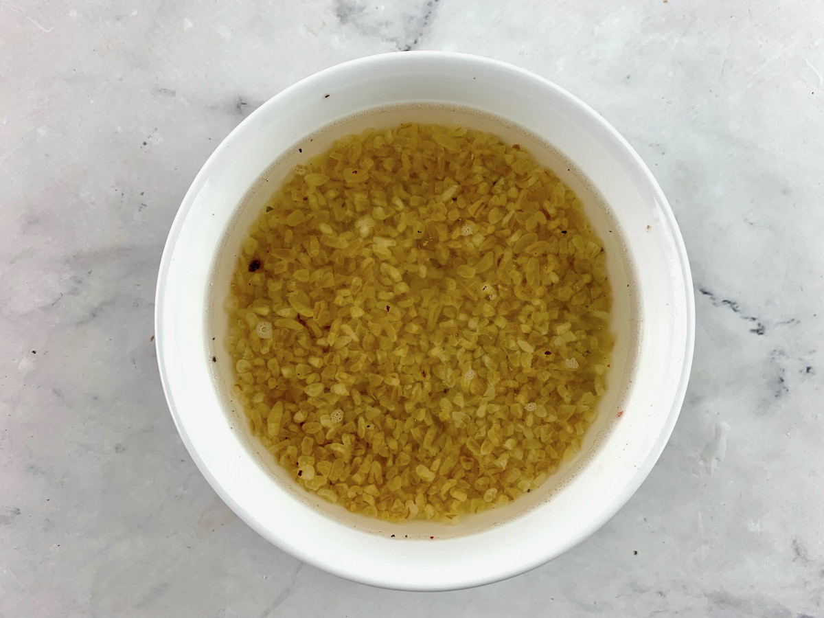Adding water to bulgur in a white bowl.