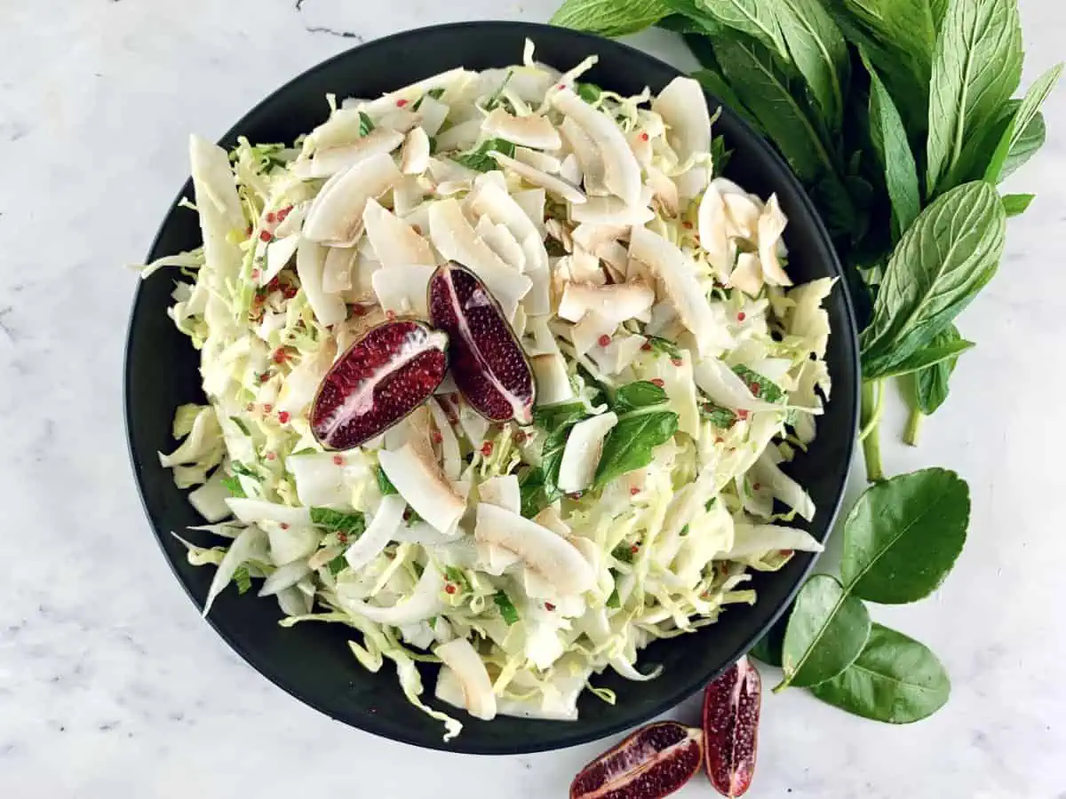 Cabbage fennel slaw in a black bowl with mint sprigs, lime leaves and halved finger limes.