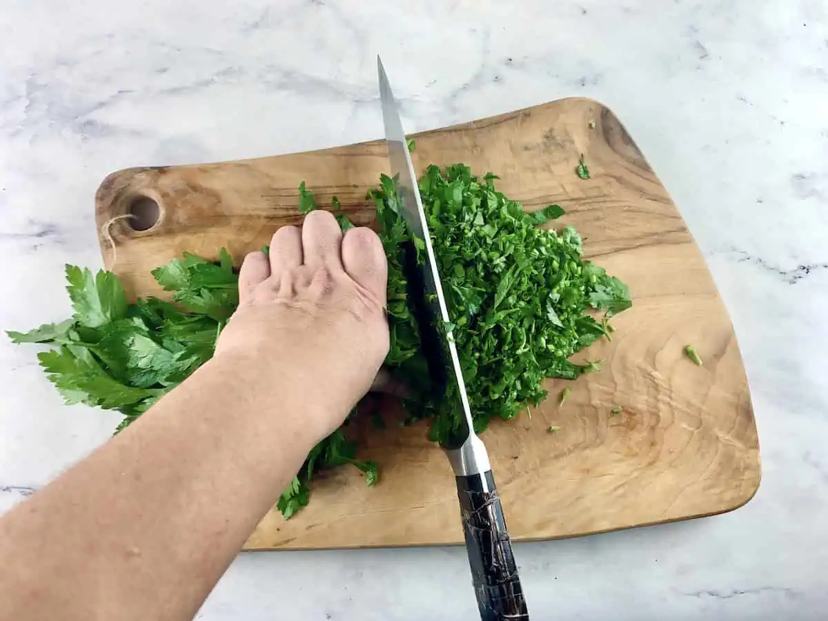 Chopping parsley on a wooden board with a large knife.