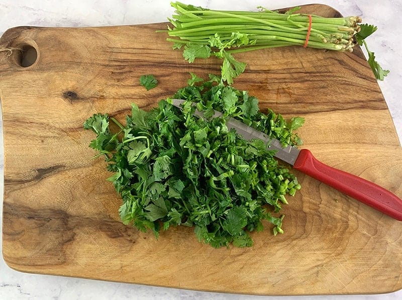 Chopped parsley on a wooden board with a knife and cut stems on the side.