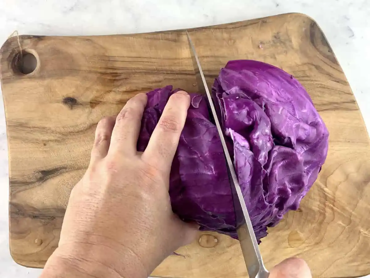 Hand cutting a red cabbage half into quarters on a wooden board.