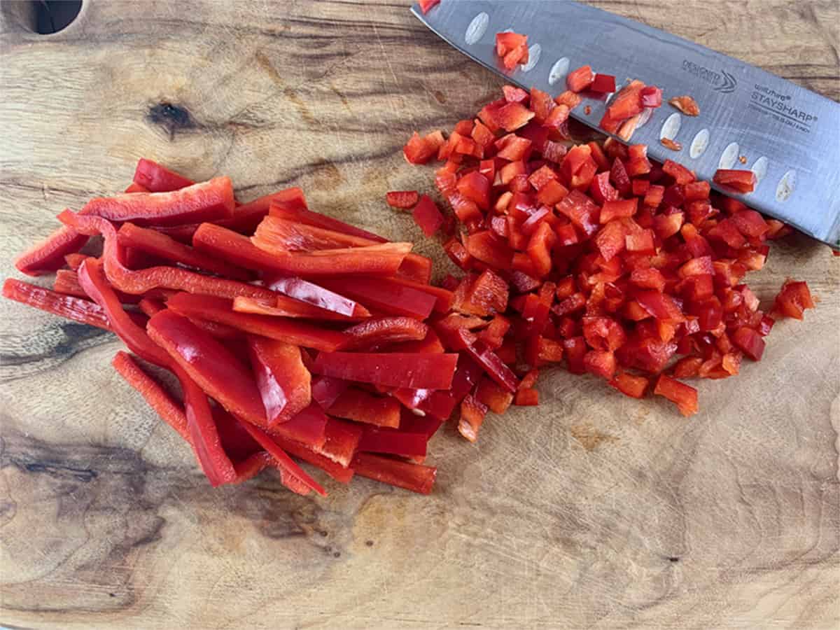 Dicing red capsicum, bell pepper on a wooden board with a knife. 