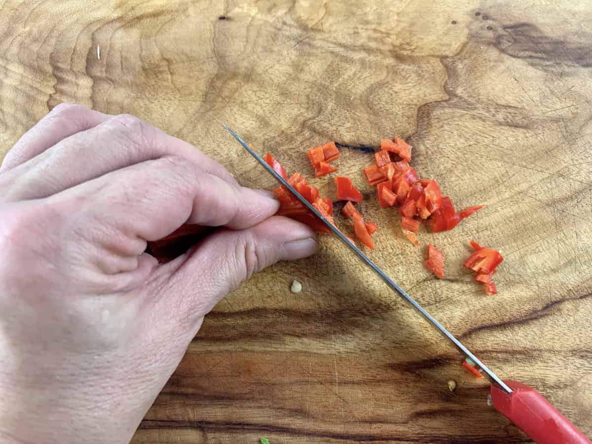 Aerial view of hands dicing red chilli on a wooden board.