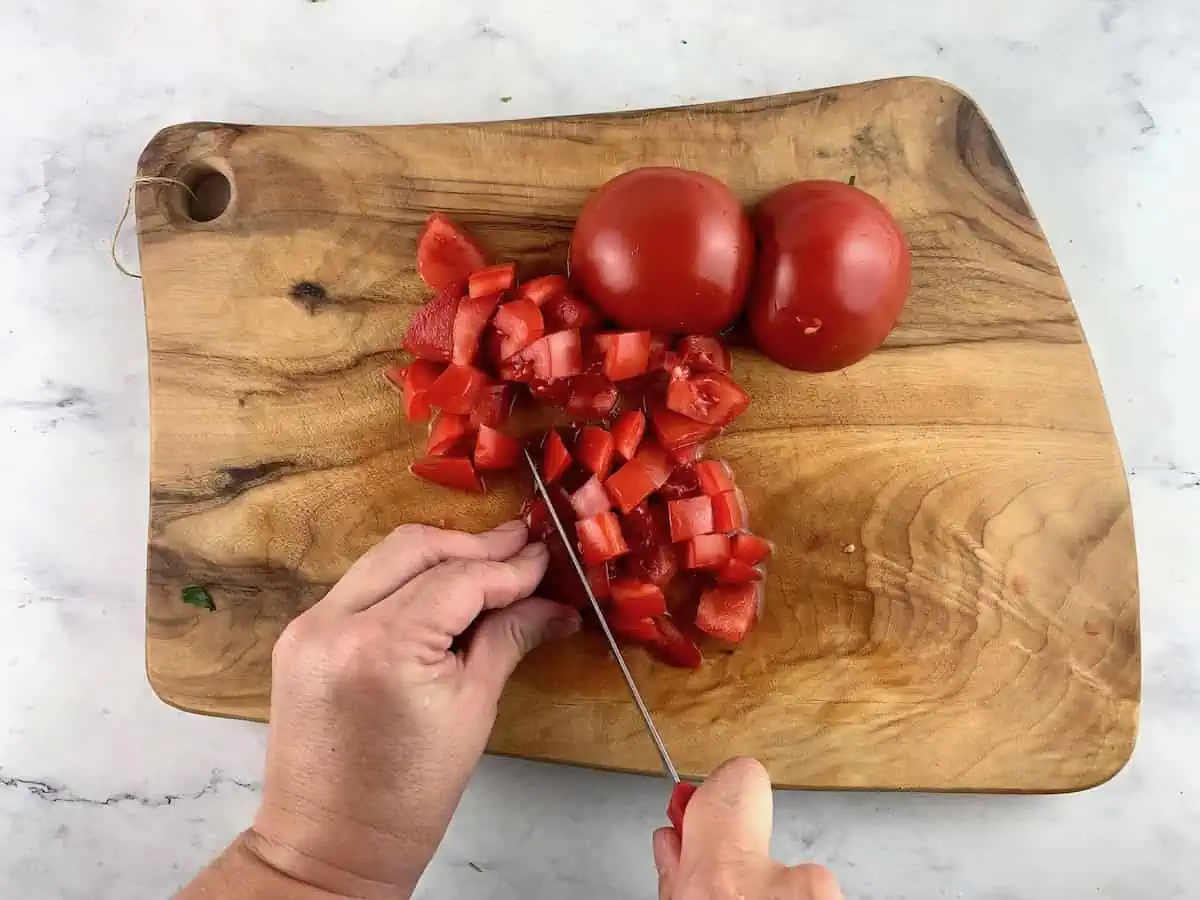 Dicing tomatoes with a serrated knife on a wooden board.