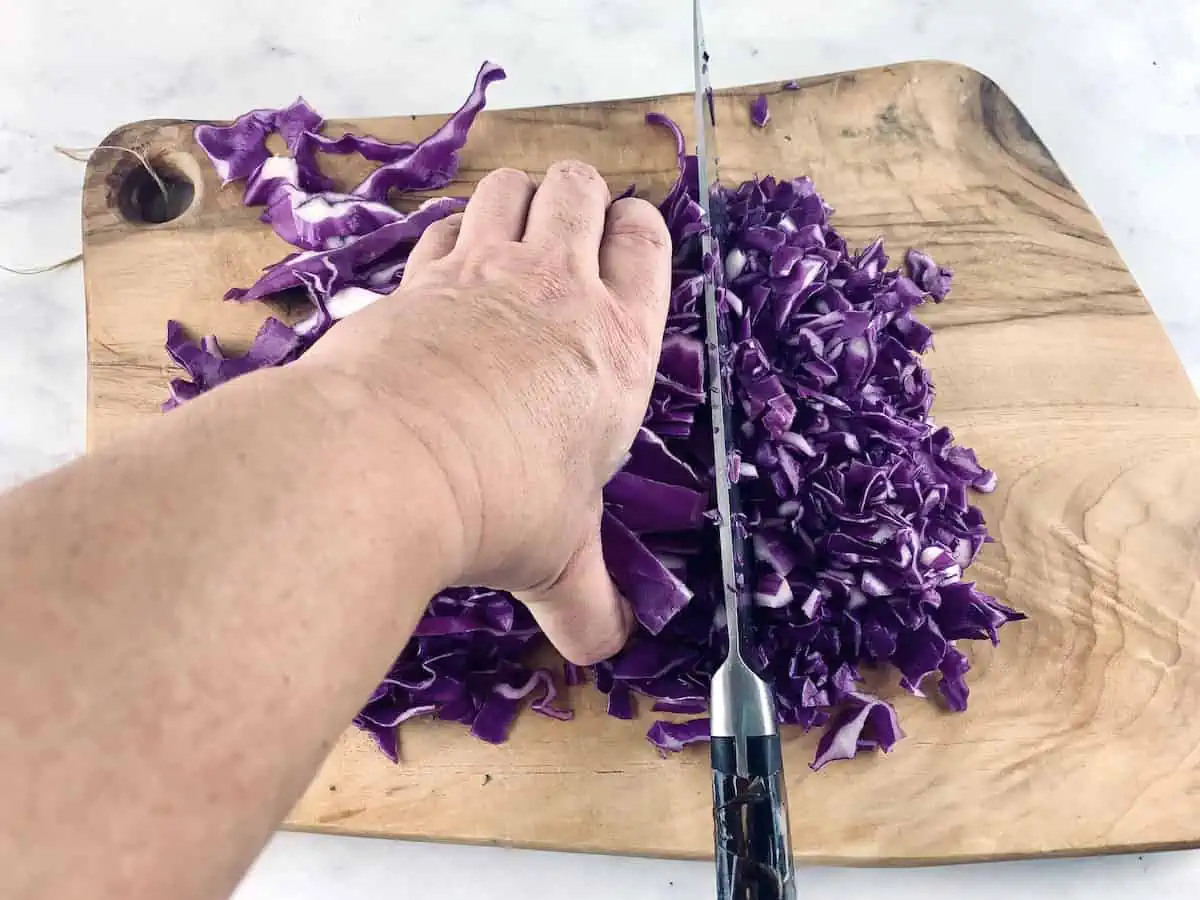 Hands dicing red cabbage on a wooden board.