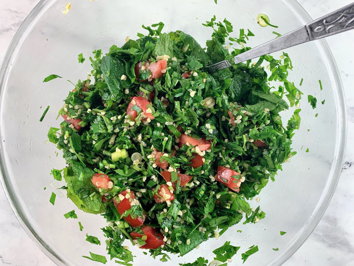 Mixing Lebanese tabbouleh in a glass bowl with a spoon.