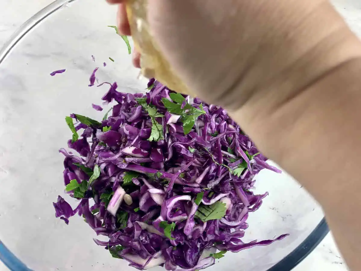 Squeezing lemon juice on red cabbage salad in a glass bowl.