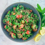 Lentil tabbouleh in a dark grey bowl with lemon halves and sprigs of mint on the side.