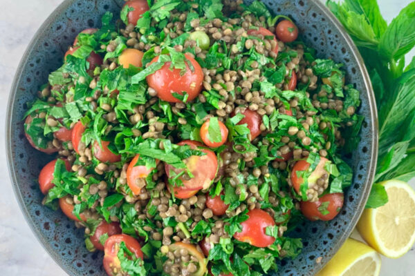 Lentil tabbouleh in a dark grey bowl with lemon halves and sprigs of mint on the side.