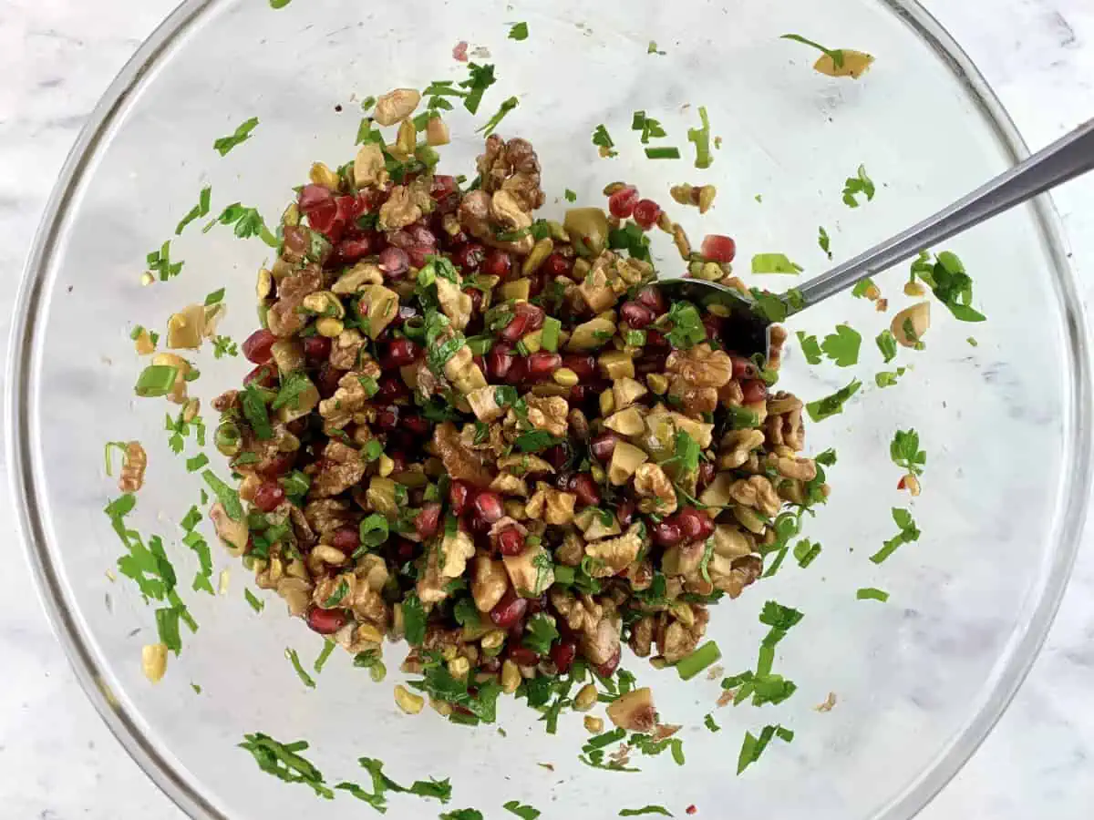 Mixing walnut pomegranate salad in a glass bowl with a spoon.