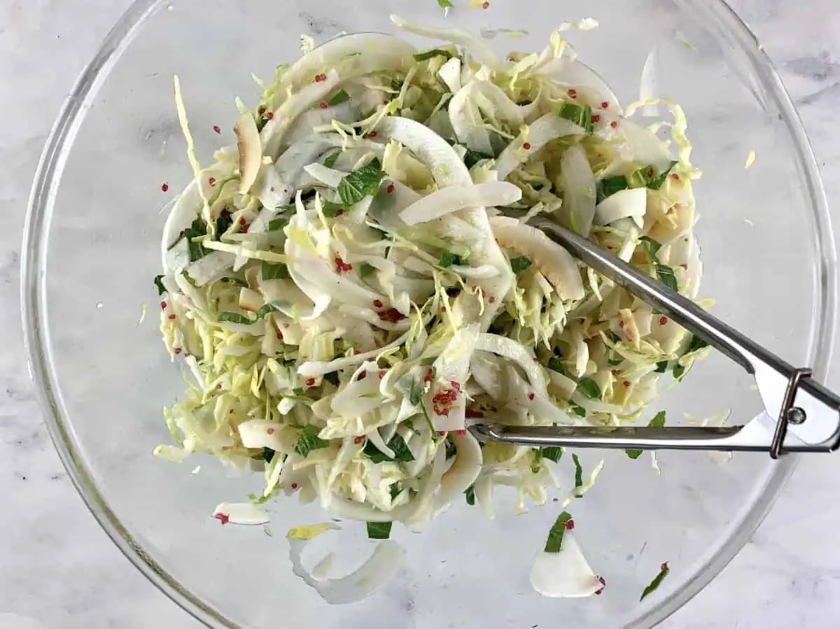 Mixing cabbage fennel slaw in a glass bowl with tongs.