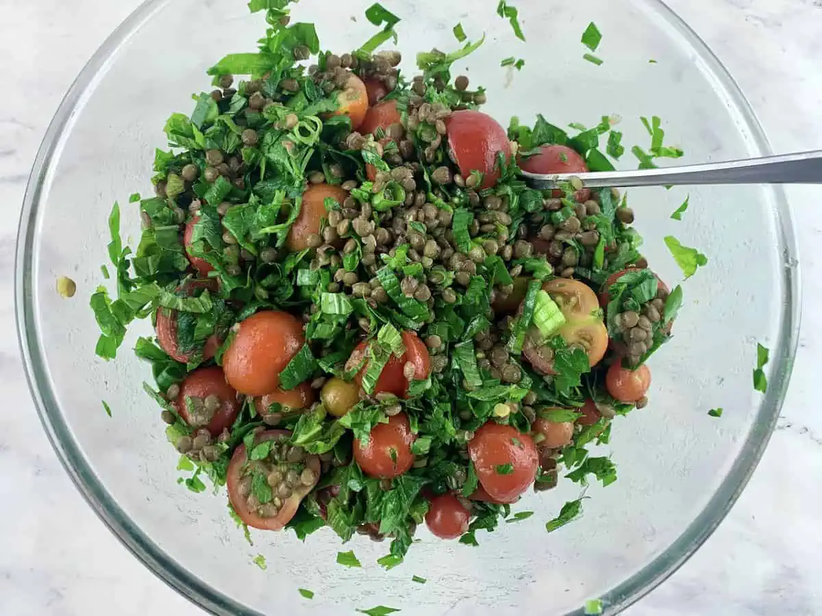 Mixing lentil tabbouleh salad in a glass bowl with a spoon.