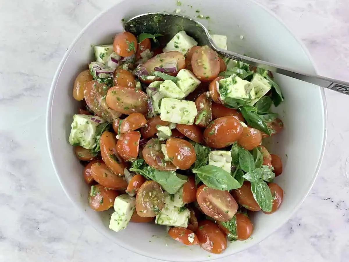 Mixing Mediterranean tomato feta salad in a white bowl with a spoon.