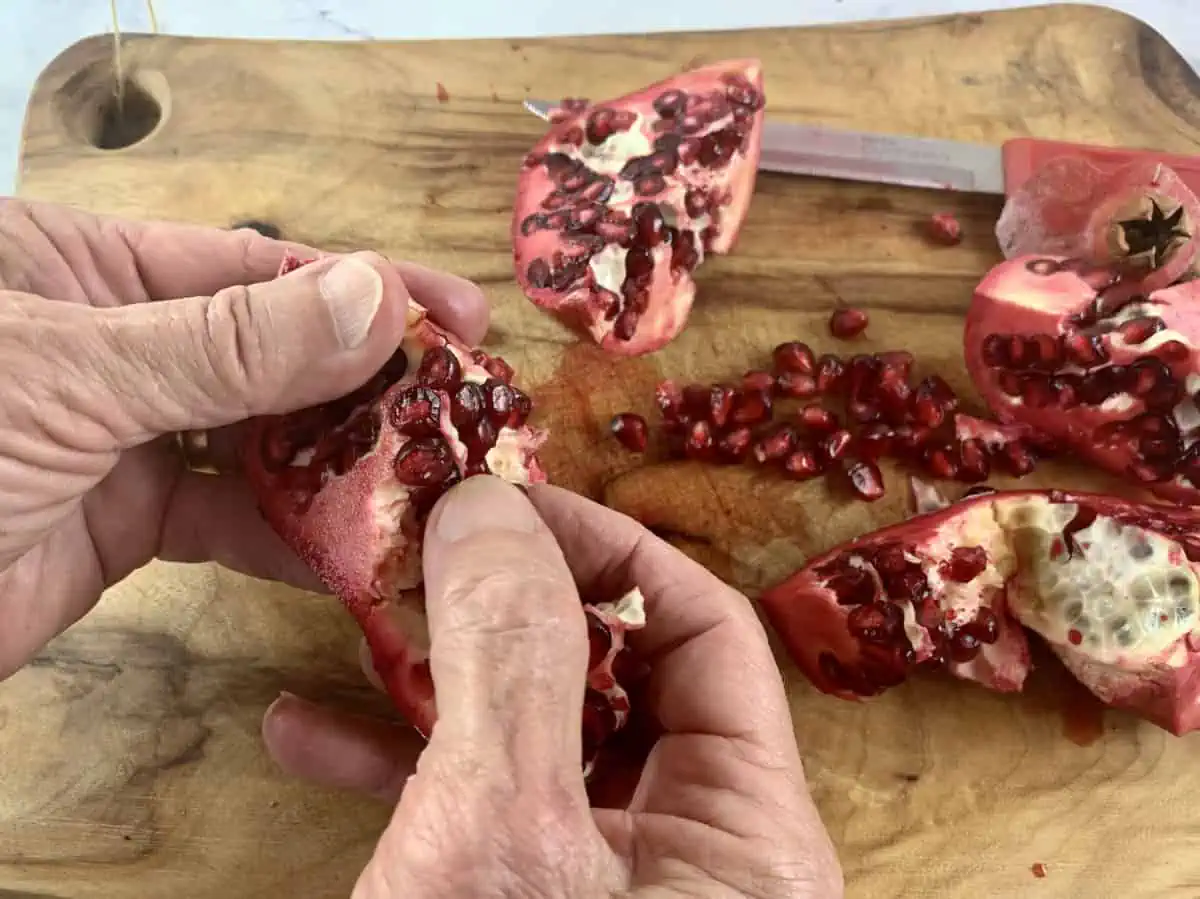 Hands dislodging pomegranate arils from the membrane.
