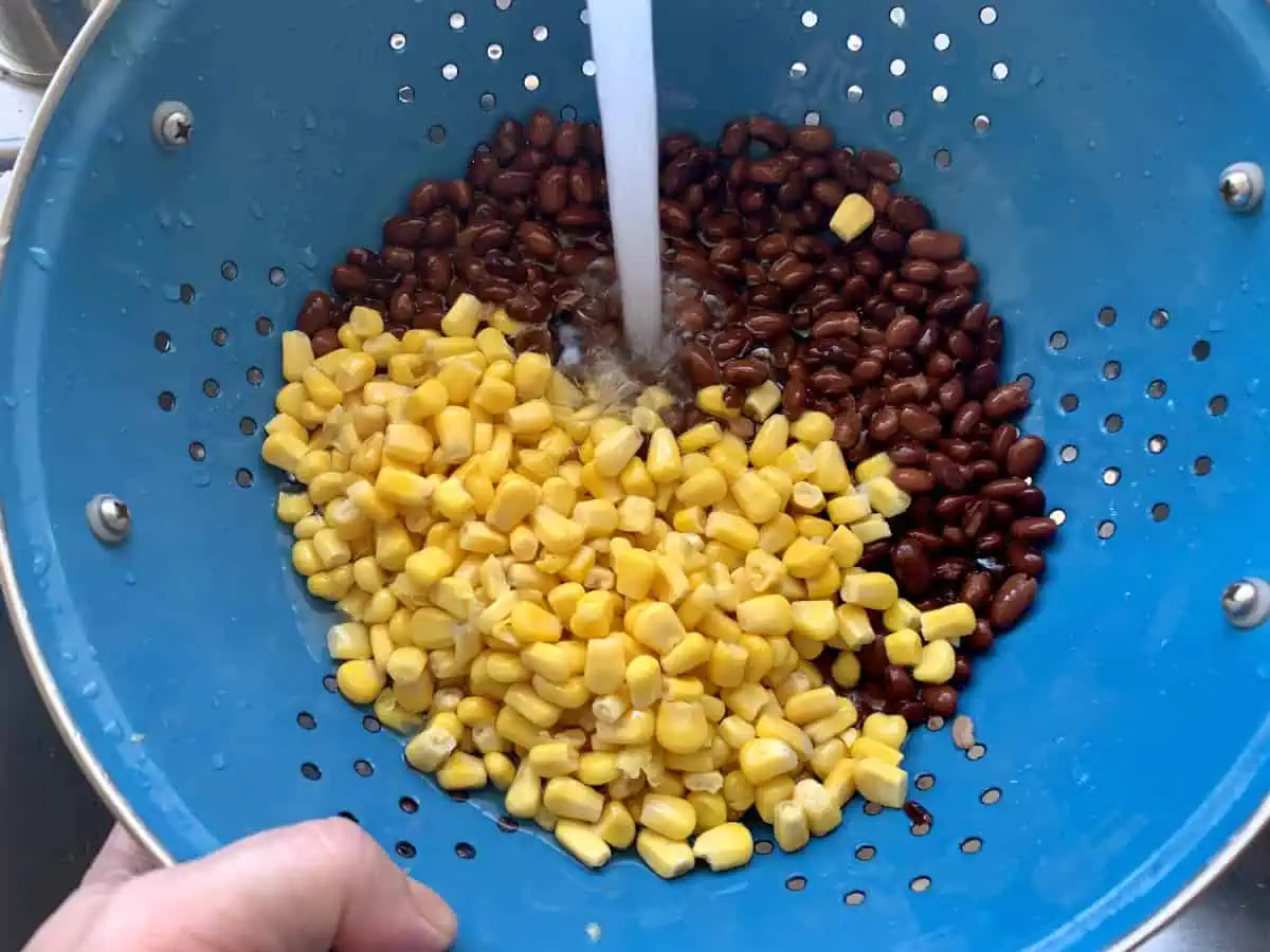 Rinsing corn and black beans in a colander under cold water in the sink.