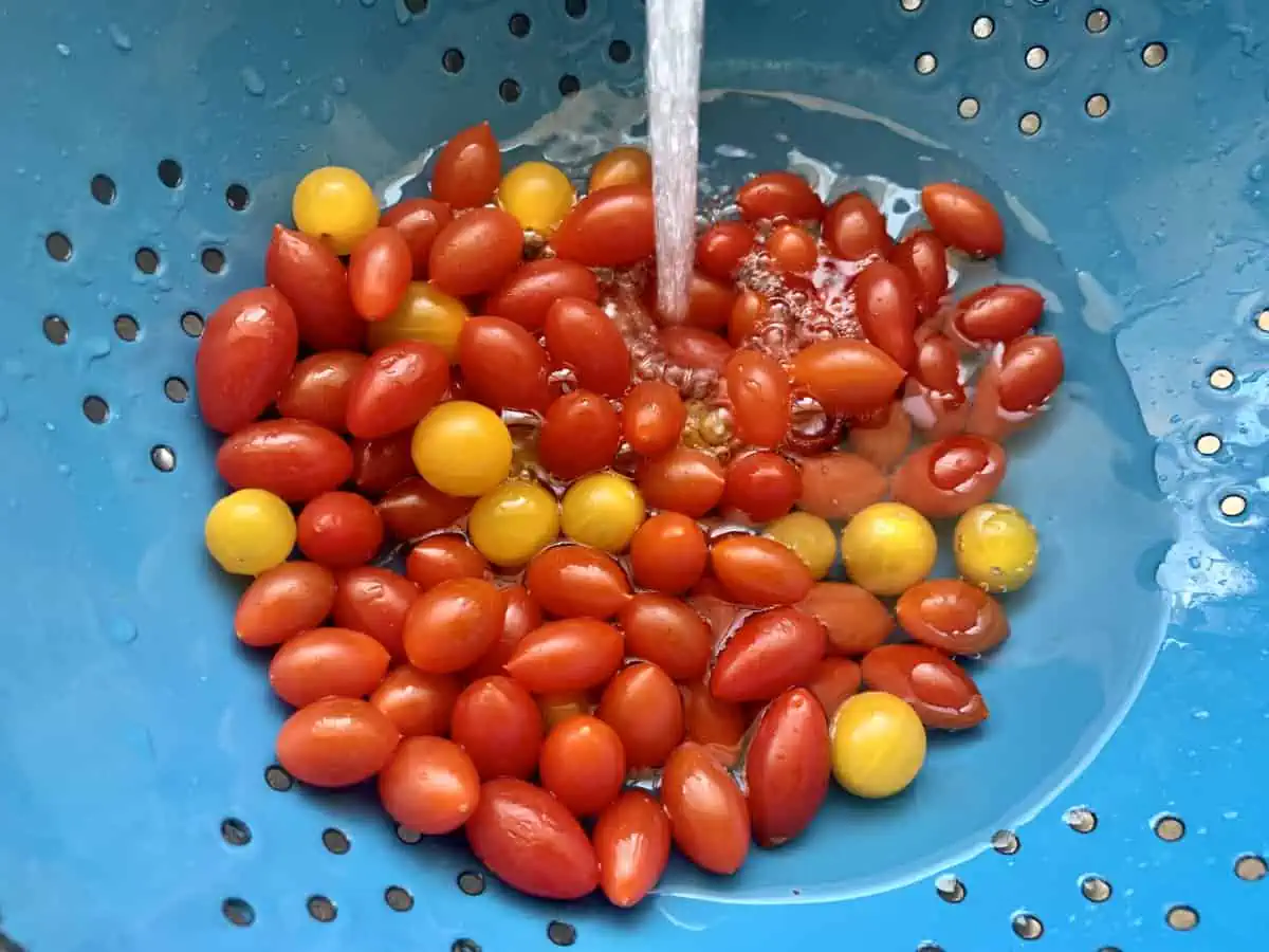 Rinsing mini tomatoes in a colander under cold water in the sink.