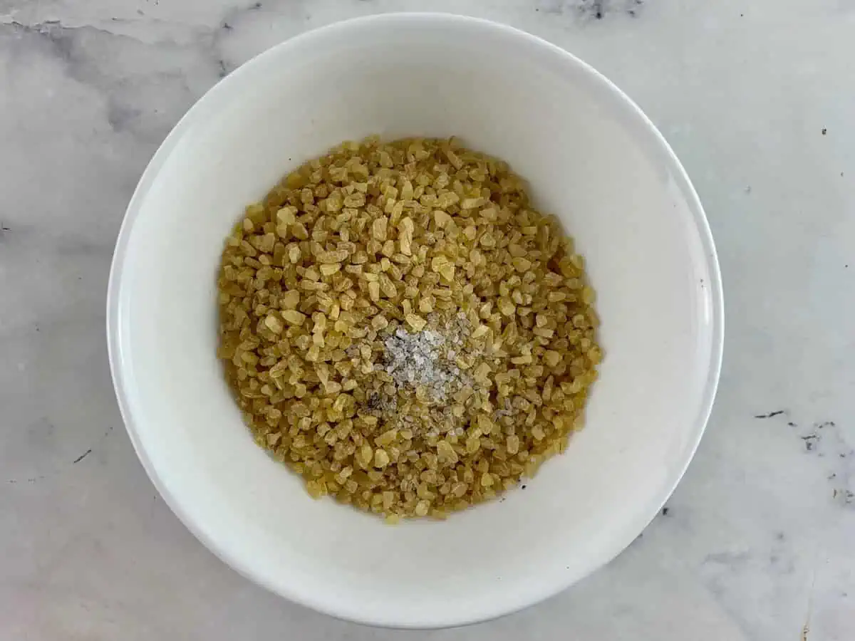 Raw bulgur that has been seasoned in a white bowl.