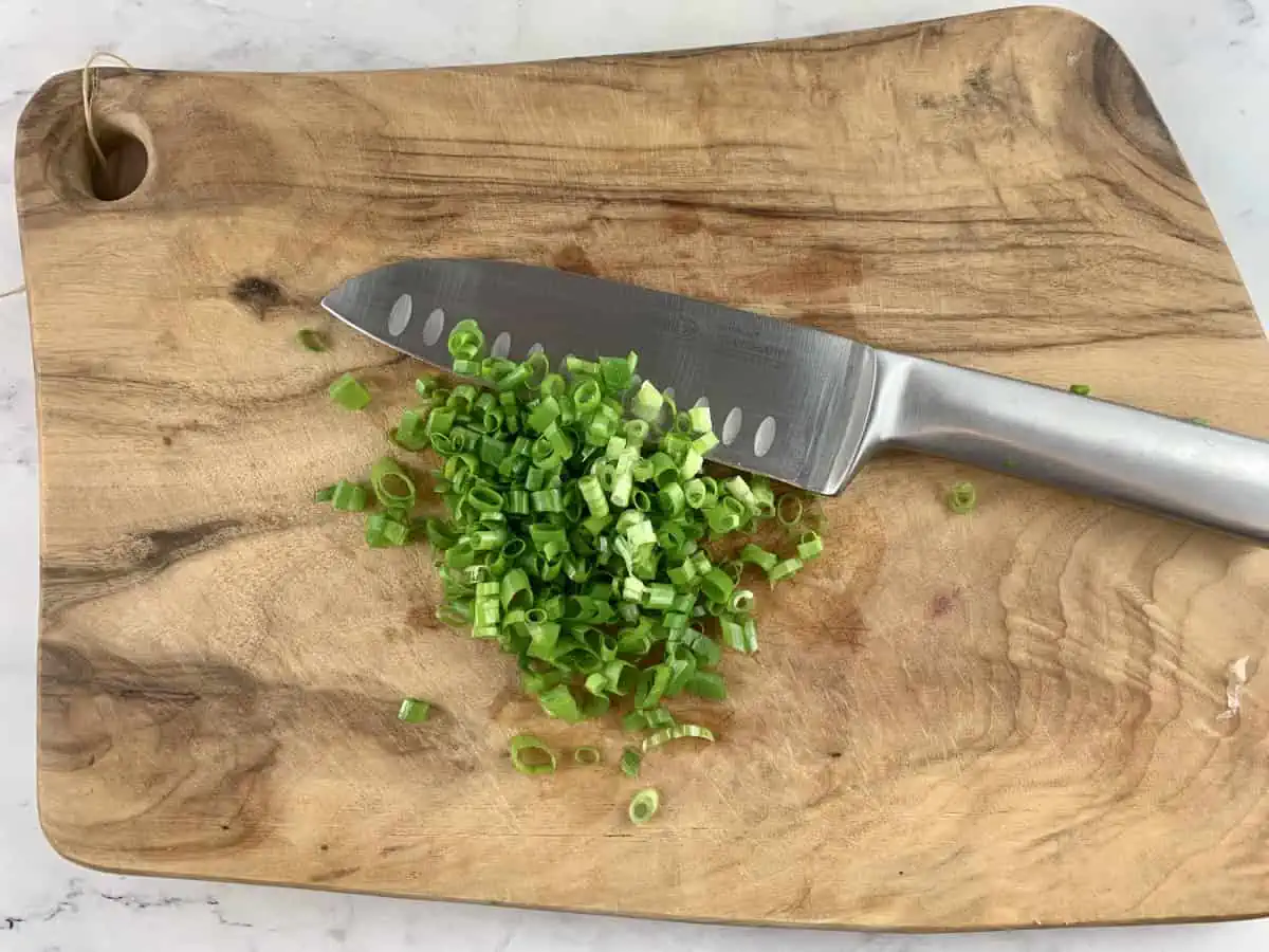Sliced green onions on a wooden chopping board with a knife.