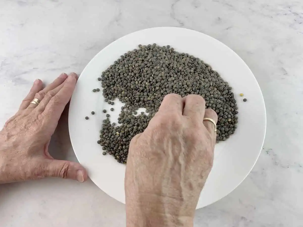 Hands sorting through lentils on a white plate.