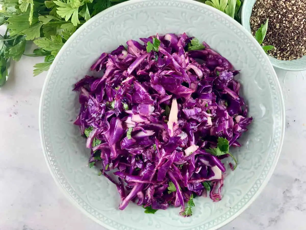 Turkish red cabbage salad in a mint coloured bowl with parsley and zaatar in a small bowl on the side.