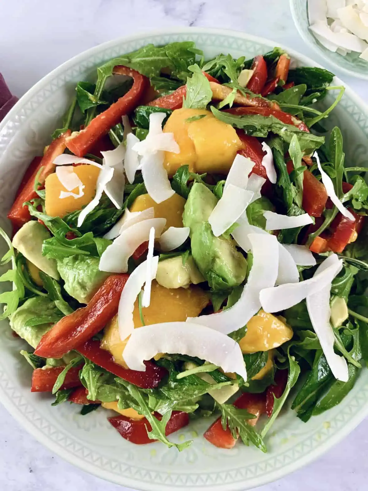 Mango avocado salad with lime dressing in a mint bowl with a blush napkin and coconut flakes on the side.