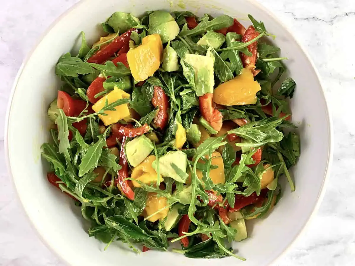 Mixing mango avocado salad with lime dressing in a white bowl.