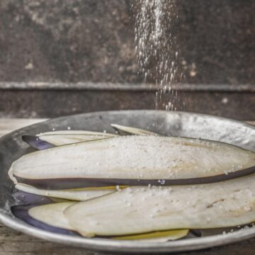 Eggplant slices on a plate with salt dropping onto them.