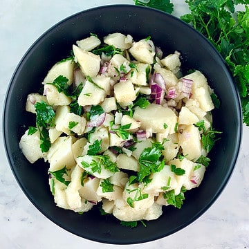 Patatosalata or Greek potato salad in a black bowl with parsley on the side.