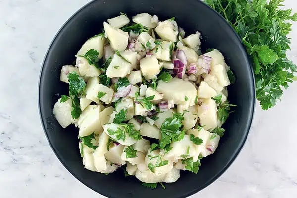 Patatosalata or Greek potato salad in a black bowl with parsley on the side.