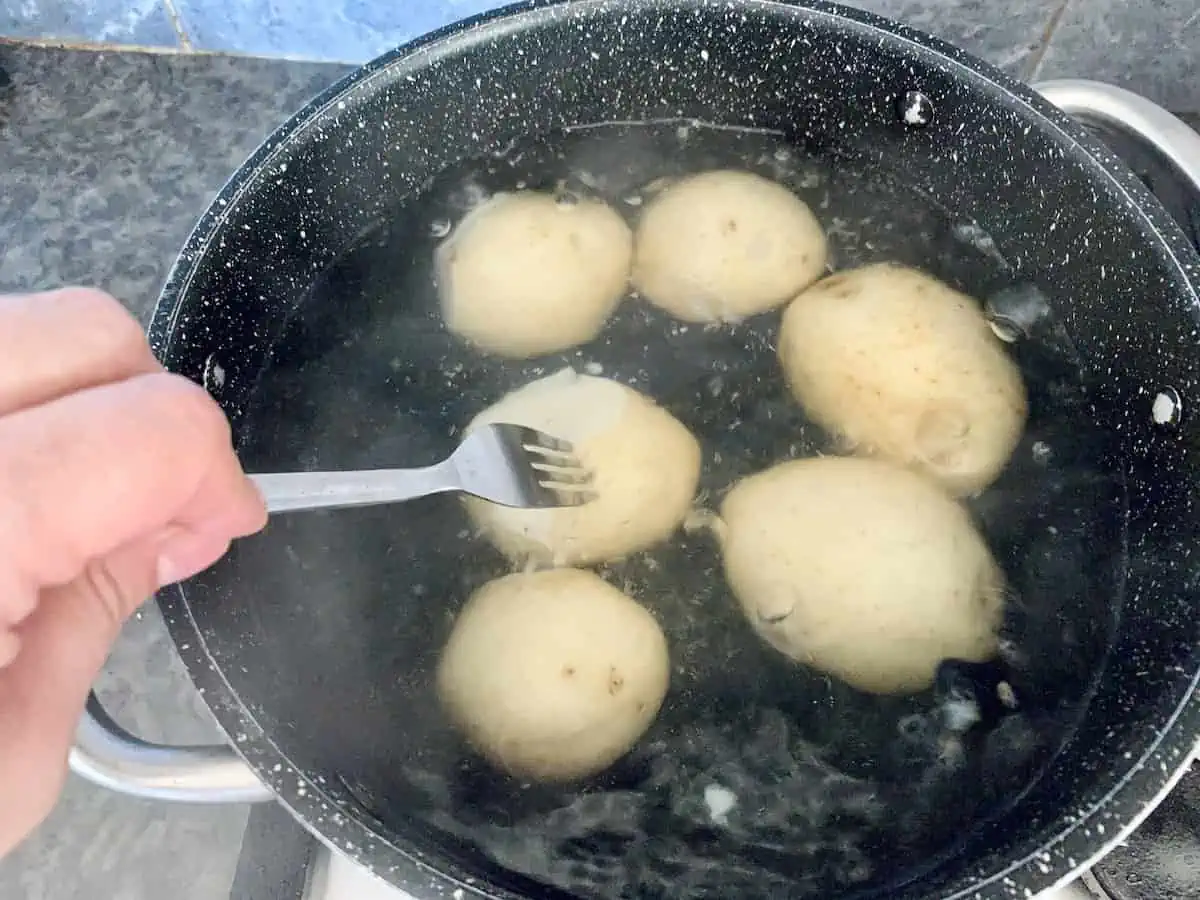 Testing boiling potatoes in a pot with a fork.