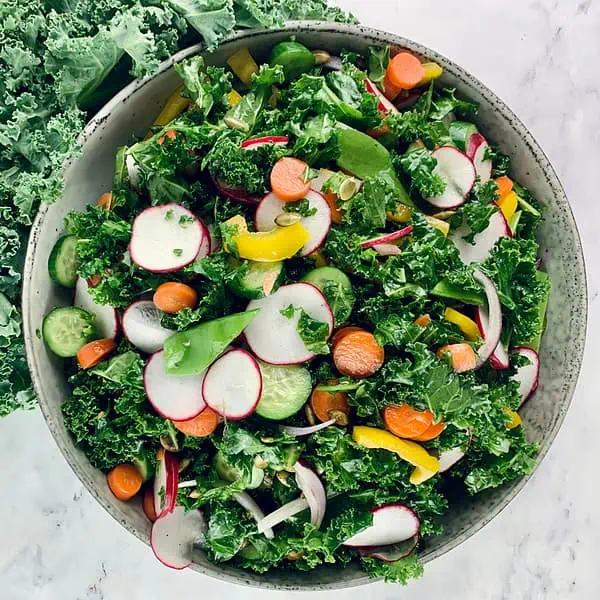 Colourful kale crunch salad in a ceramic bowl with curly kale on the side.
