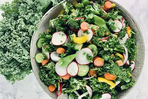Colourful kale crunch salad in a ceramic bowl with curly kale on the side. a