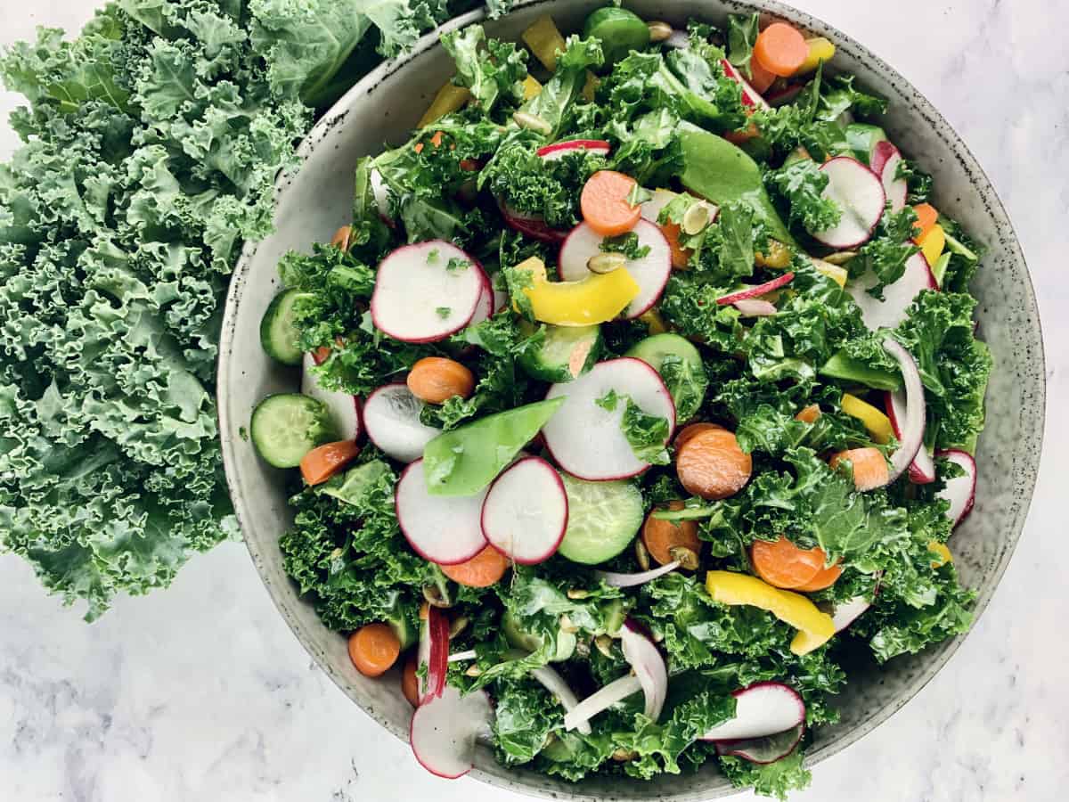 Colourful kale crunch salad in a ceramic bowl with curly kale on the side. a