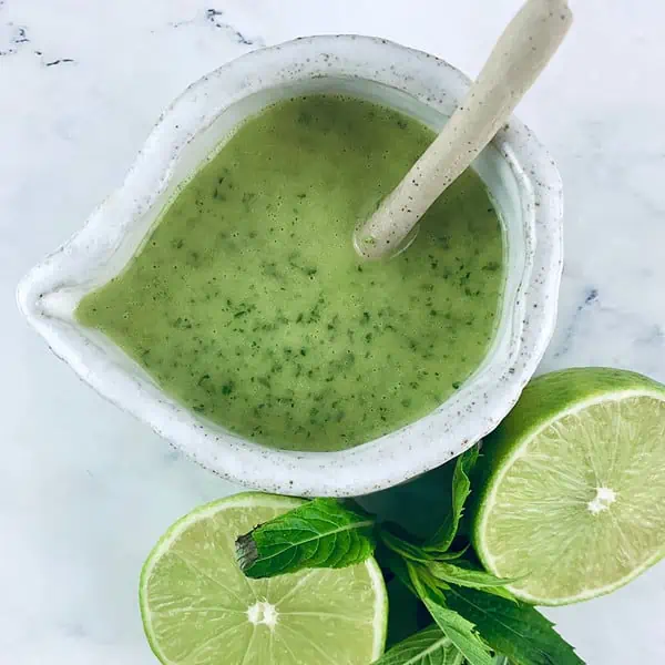 Mint Lime Dressing in a ceramic jug with a spoon with a halved lime and mint leaves.